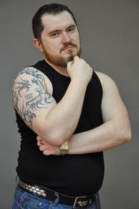 Portrait of confident man with hand on chin standing against gray background