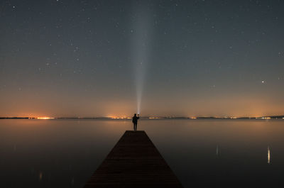 Man standing on pier over lake against sky at night