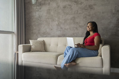Young black woman working at home with laptop on her lap sitting on her couch  notebook for working. 