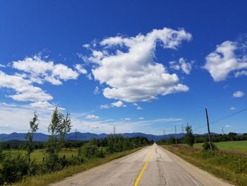 Road by trees against blue sky