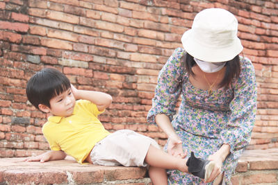 Full length of couple sitting against brick wall