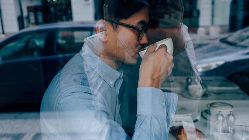 Man drinking coffee sitting at table seen through glass