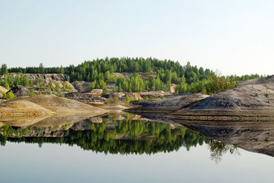 View on a flooded quarry with blue water and reflection of hills and forest.