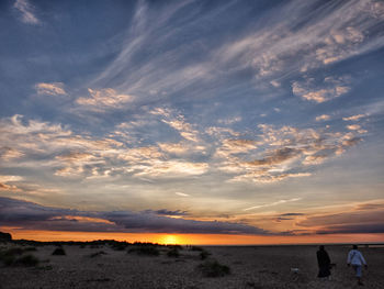 People walking at beach against sky during sunset