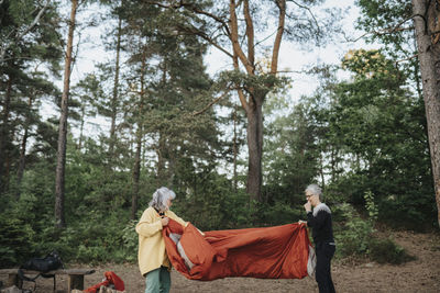 Two senior women setting up tent in forest