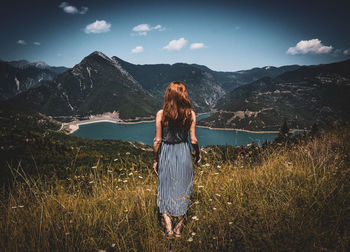 Woman standing on mountain against sky, staring at a lake