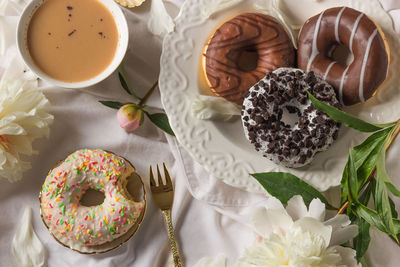 Breakfast in bed with various delicious glazed donuts on the plate, cup of coffee and peony flowers.