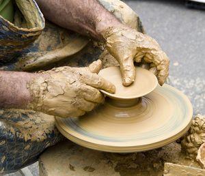 Cropped hands making earthenware on pottery wheel