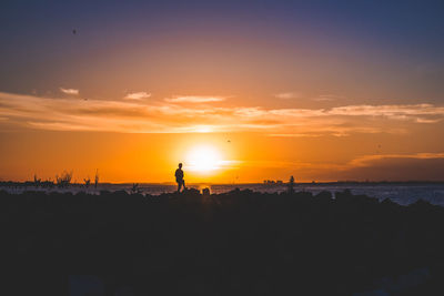 Silhouette person standing at beach against sea and sky during sunset