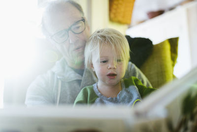 Low angle view of grandfather with granddaughter reading book while sitting at home