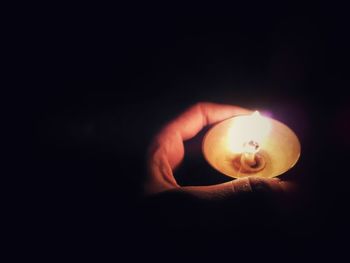 Close-up of hand holding illuminated candle against black background