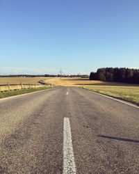 Road passing through field against clear sky