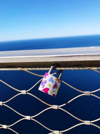 Padlocks hanging on railing by sea against sky