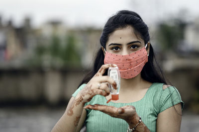 Close-up of woman wearing red mask using hand sanitizer