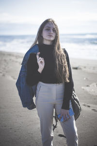 Portrait of teenage girl standing at beach against sky