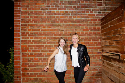 Full length portrait of happy friends standing against brick wall