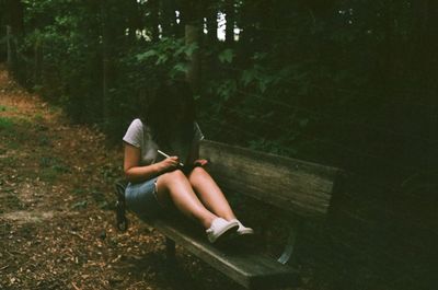Side view of woman sitting on bench in forest