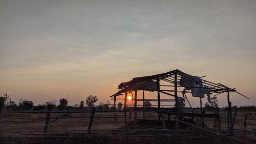 Silhouette traditional windmill on field against sky during sunset