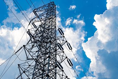 Low angle view of electricity pylon against blue sky