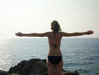 Rear view of man standing on rock by sea against sky