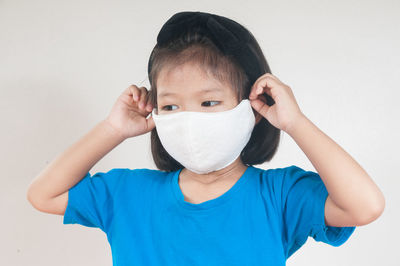 Close-up of cute girl wearing mask standing against white background