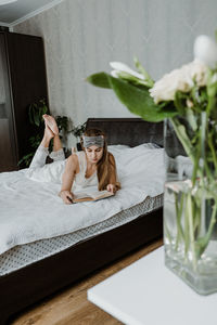 Young woman lying on bed while reading book