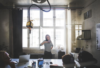 Businesswoman looking at mobile phone while standing against windows in board room