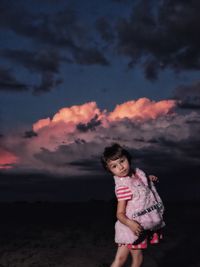 Portrait of girl standing on field against cloudy sky during sunset