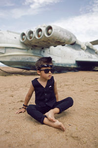 Rocker boy a child in black clothes stands against the background of an abandoned plane 