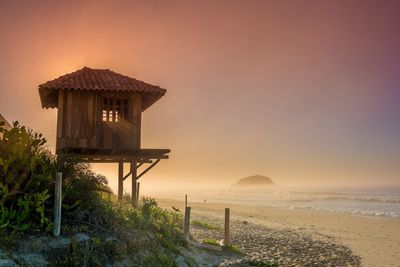 Lifeguard hut on beach against sky during sunset