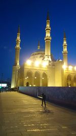 Man walking in illuminated temple against clear sky at night