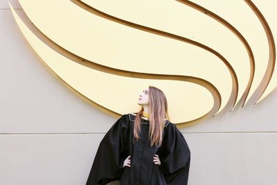 Young woman looking away while standing against wall