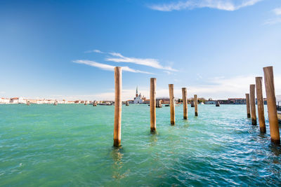 Wooden posts in sea against blue sky