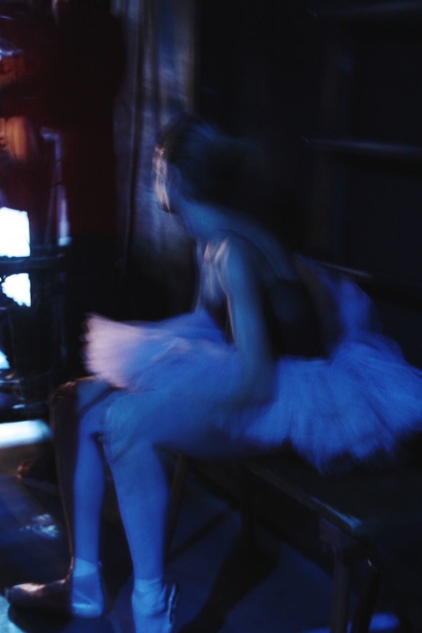 BLURRED MOTION OF WOMAN SITTING ON CHAIR IN NIGHTCLUB