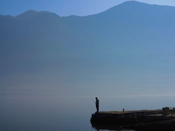 Silhouette man standing on mountain by sea against sky