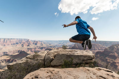 Full length of man jumping over cliff against sky