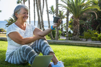 Smiling senior woman taking selfie while sitting at park