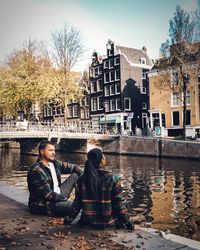 Couple sitting by canal against buildings