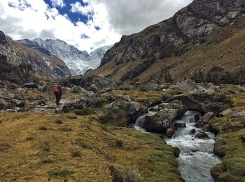 Hiker walking on mountain against cloudy sky