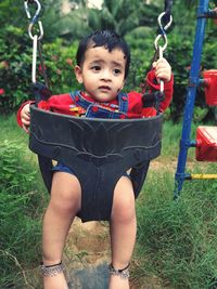 Cute girl looking away while sitting in swing at playground