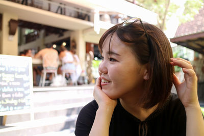 Smiling woman with hands on chin looking away while sitting at outdoor cafe