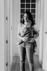 Smiling mother holding daughter at entrance of home