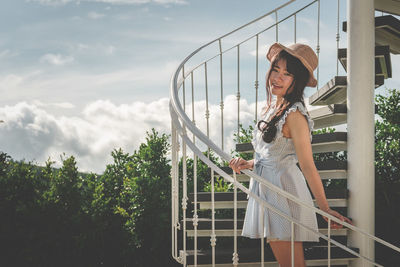 Side view of woman standing by railing against sky