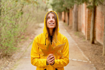 Woman holding autumn leaf on footpath