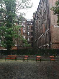 Empty bench by building in city against sky