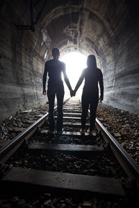 Rear view of silhouette people standing on railroad track