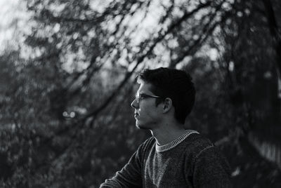 Side view of young man wearing eyeglasses standing in field