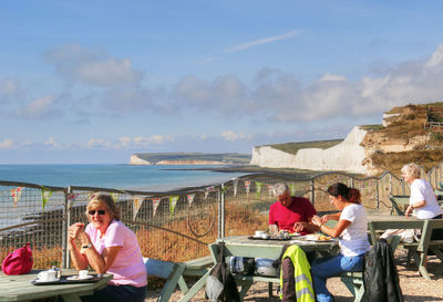 People sitting on table by sea against sky