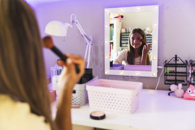 Girl applying make-up with brush looking in mirror at home