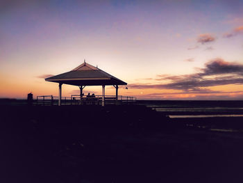 Silhouette lifeguard hut on beach against sky during sunset